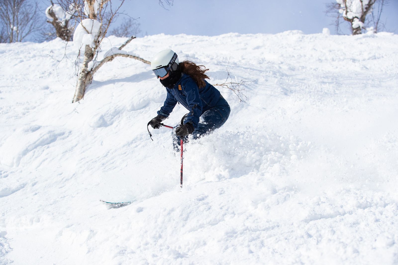 FES skier carving a stylish turn through powder under blue sky in Niseko